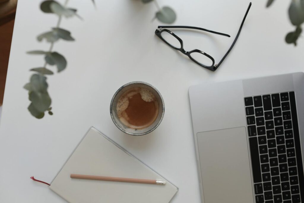 From above of cup with hot drink near netbook and notepad under plant