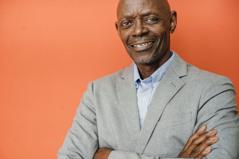 Crop glad middle aged male entrepreneur in formal apparel with folded arms looking at camera with toothy smile